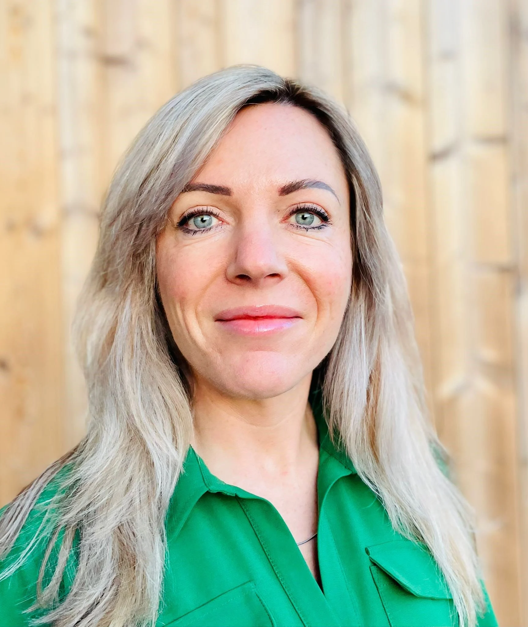 Annelies van Oosterom, International Business Development Manager for Food, Feed, and Agriculture, with long blonde hair, wearing a green shirt, standing in front of a wooden background