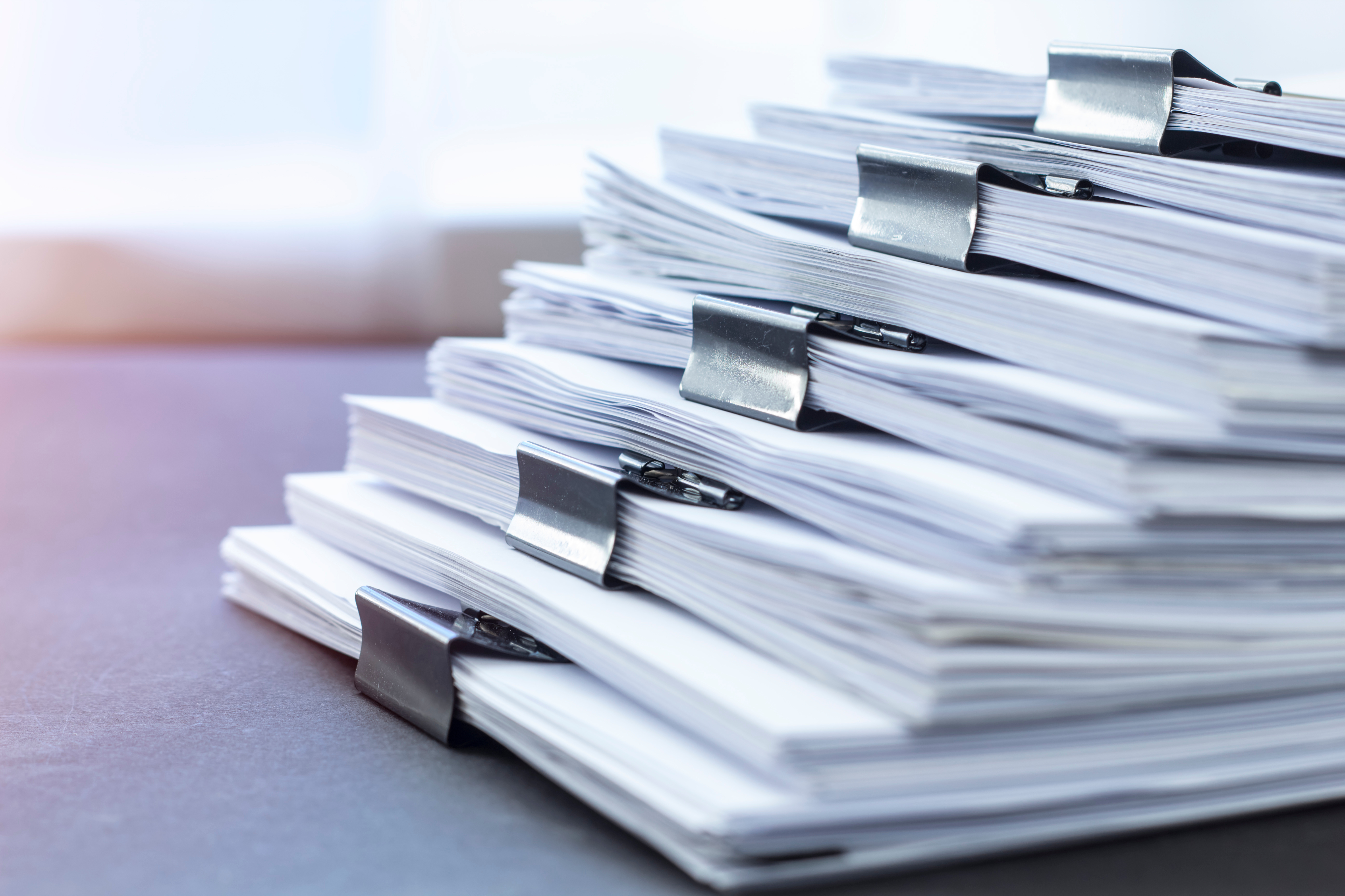 Stack of paper documents secured with binder clips on a desk, symbolizing office work and organization