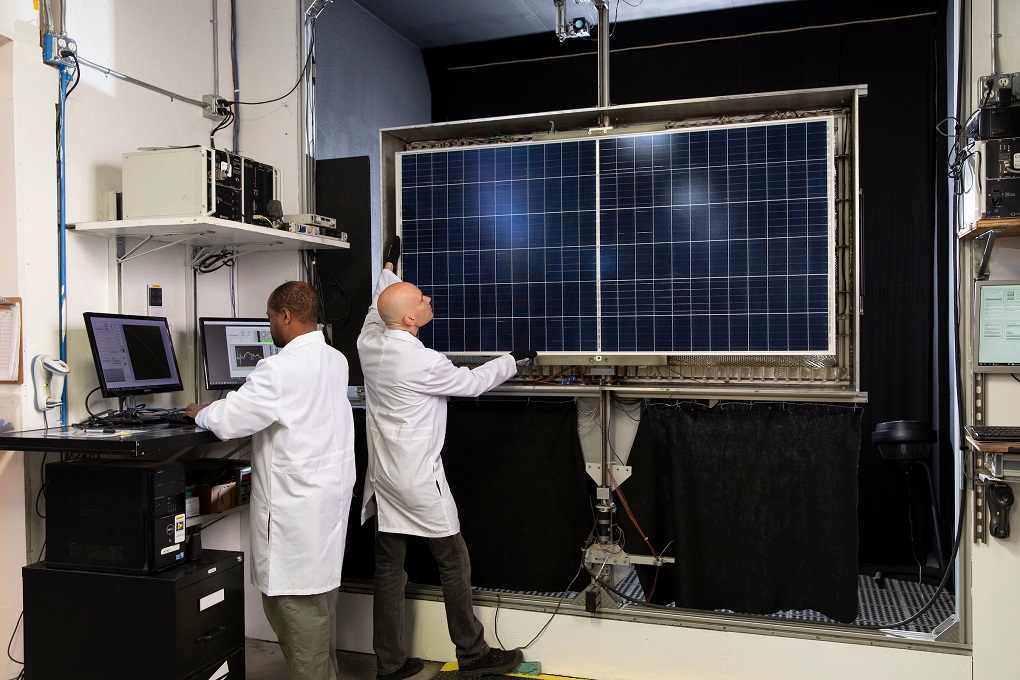 Two Kiwa PVEL Laboratory employees in white lab coats conducting tests on a large solar panel inside a laboratory.