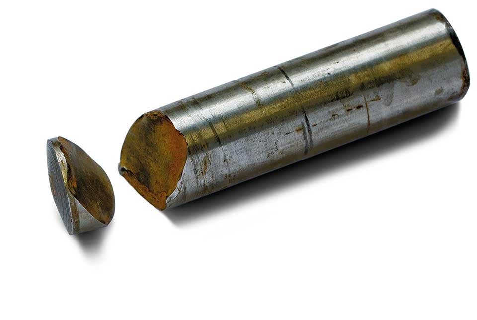 Bruten metallstav vid förstörande provning med en slät yta och rostbeläggning vid kanten.