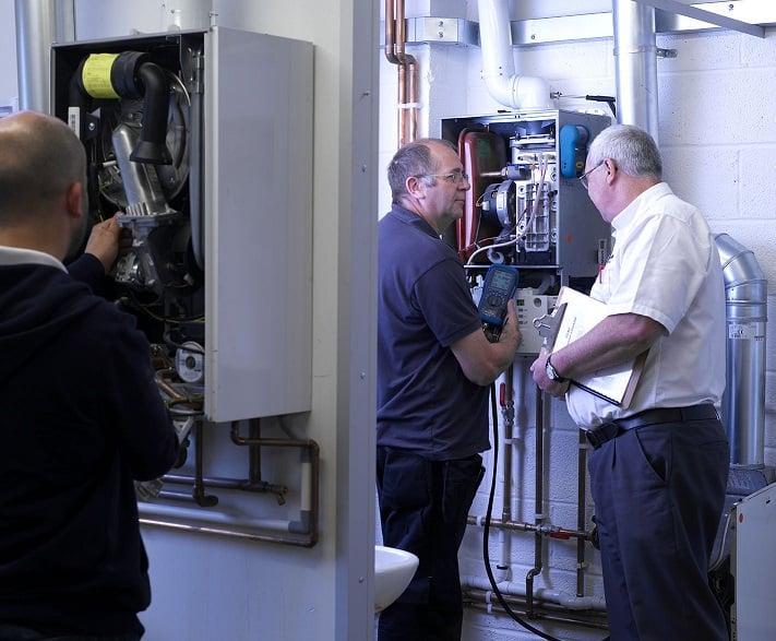 Kiwa trainer and student inspecting and repairing industrial boilers in a utility room